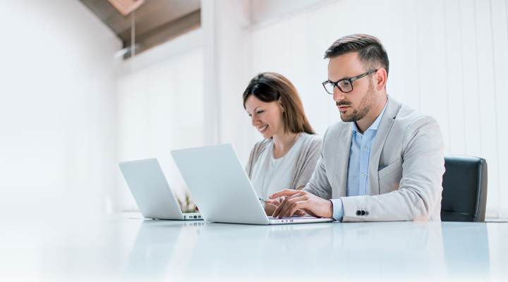 Two administrators are managing devices using LG SuperSign Control+ on personal PCs.